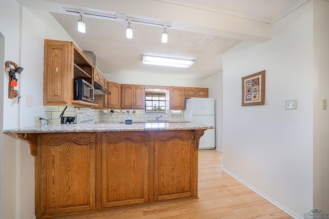 kitchen featuring kitchen peninsula, track lighting, light stone counters, light hardwood / wood-style floors, and white fridge