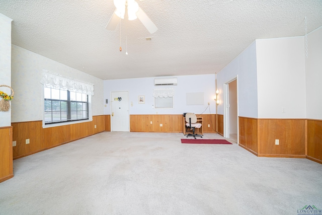 carpeted empty room with a textured ceiling, a wall unit AC, and ceiling fan