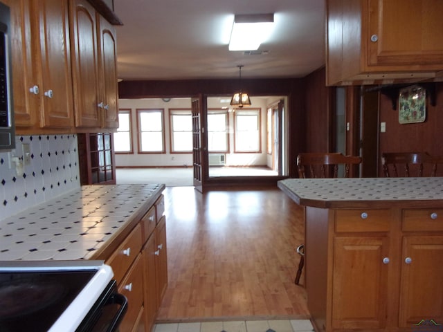 kitchen with tile countertops, electric range, brown cabinetry, and light wood finished floors