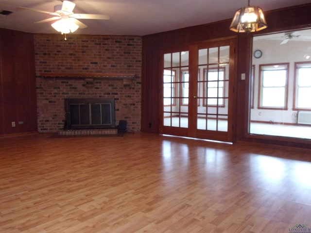 unfurnished living room with a brick fireplace, a ceiling fan, and wood finished floors