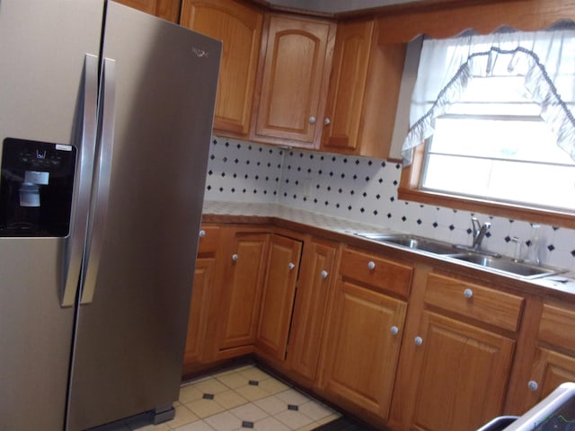 kitchen with brown cabinets, backsplash, stainless steel refrigerator with ice dispenser, and a sink