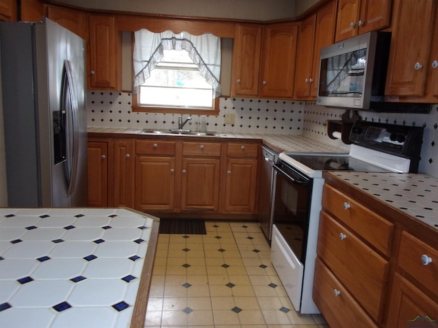 kitchen featuring tile countertops, brown cabinets, a sink, stainless steel appliances, and backsplash
