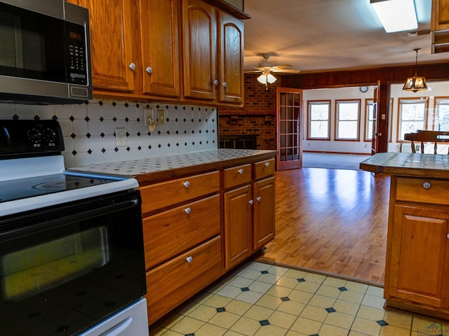 kitchen featuring tile counters, stainless steel microwave, brown cabinets, and electric range oven