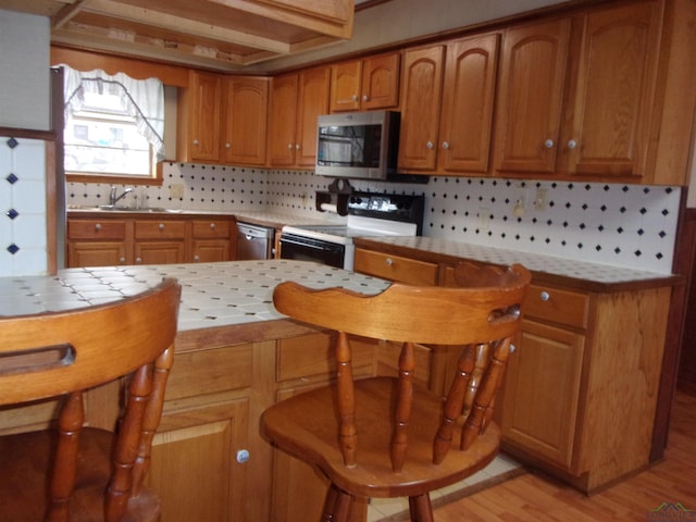 kitchen featuring tasteful backsplash, appliances with stainless steel finishes, brown cabinets, light wood-style floors, and a sink