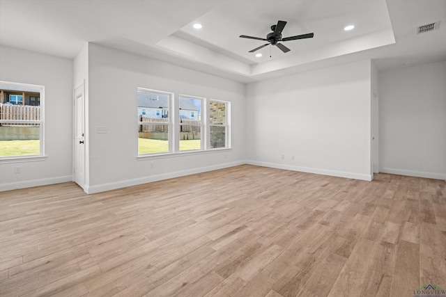 empty room featuring ceiling fan, a tray ceiling, and light hardwood / wood-style floors