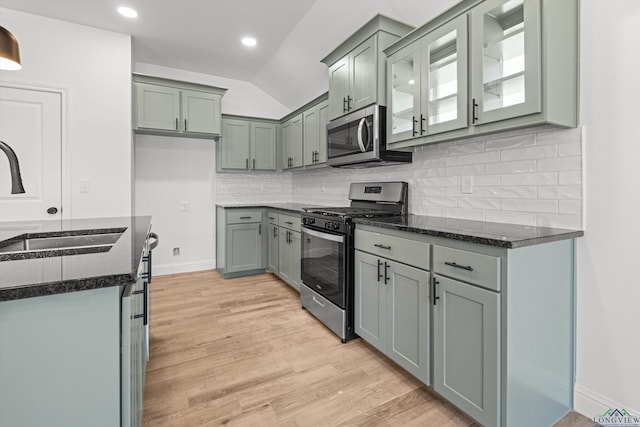 kitchen with appliances with stainless steel finishes, tasteful backsplash, lofted ceiling, dark stone counters, and sink