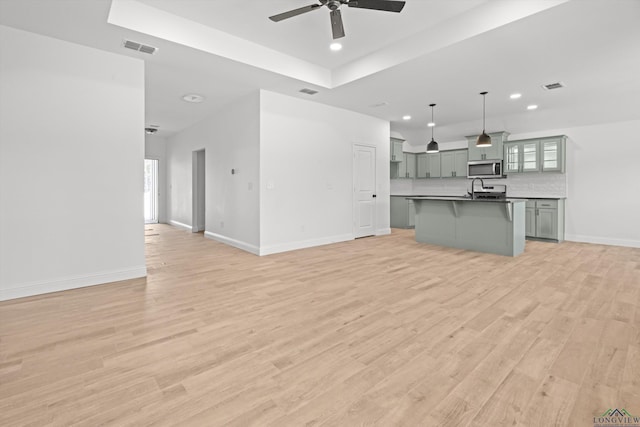 unfurnished living room with ceiling fan, sink, a tray ceiling, and light wood-type flooring