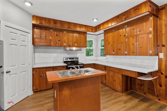 kitchen featuring sink, backsplash, light hardwood / wood-style floors, stainless steel range with electric stovetop, and a center island with sink