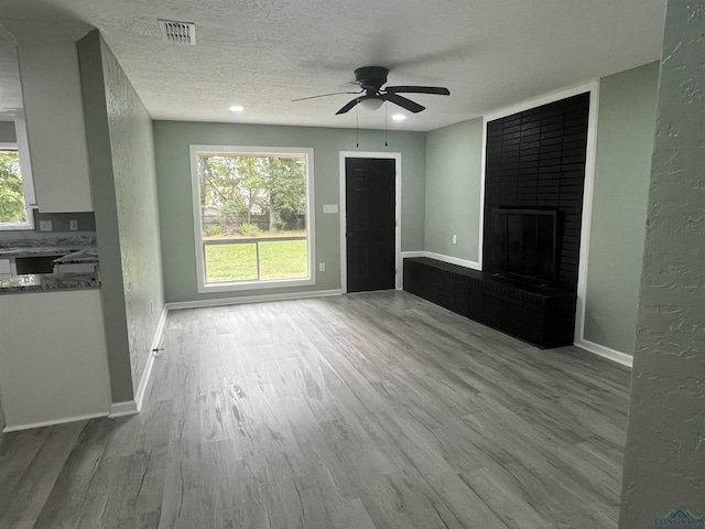 unfurnished living room featuring ceiling fan, light hardwood / wood-style floors, a textured ceiling, and a brick fireplace