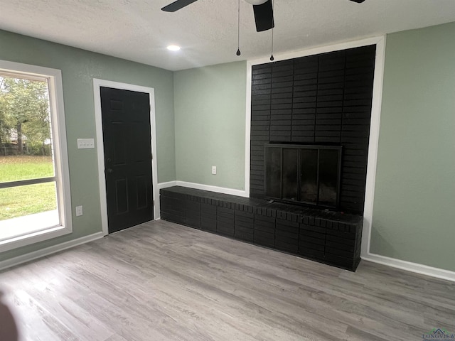 unfurnished living room featuring plenty of natural light, light wood-type flooring, a textured ceiling, and a brick fireplace