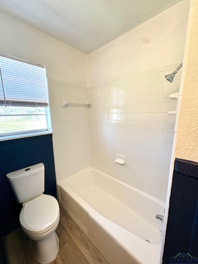 bathroom featuring toilet, wood finished floors, shower / bathtub combination, and a textured ceiling