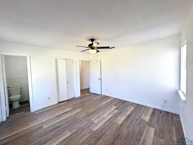unfurnished bedroom with ceiling fan, baseboards, wood finished floors, and ensuite bathroom