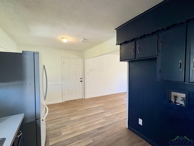 kitchen featuring visible vents, crown molding, light wood-style flooring, freestanding refrigerator, and a textured ceiling