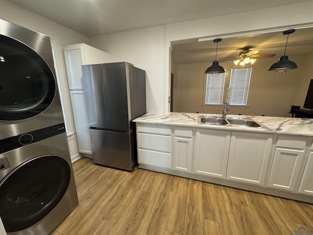 kitchen featuring hanging light fixtures, sink, stacked washer and dryer, white cabinetry, and stainless steel refrigerator