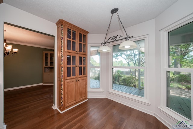 unfurnished dining area featuring crown molding, dark wood-type flooring, a textured ceiling, and a notable chandelier