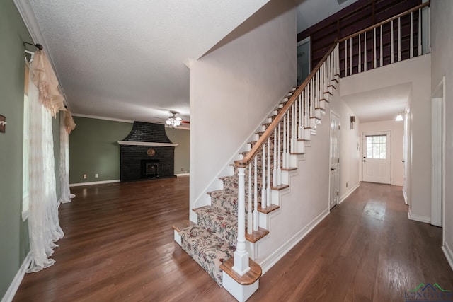 staircase featuring ornamental molding, a textured ceiling, ceiling fan, hardwood / wood-style flooring, and a fireplace