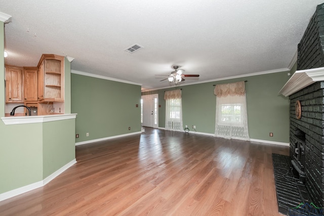 unfurnished living room with crown molding, a brick fireplace, ceiling fan, light wood-type flooring, and a textured ceiling