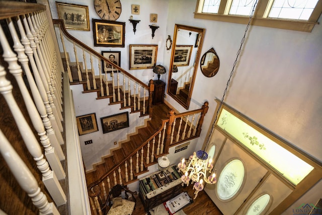 staircase with hardwood / wood-style floors, a towering ceiling, and a notable chandelier