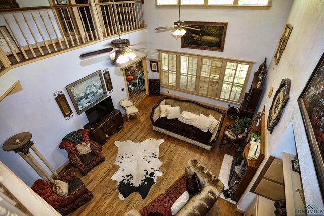 living room with ceiling fan, wood-type flooring, and a high ceiling