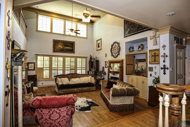 living room with ceiling fan, a fireplace, wood-type flooring, and a high ceiling