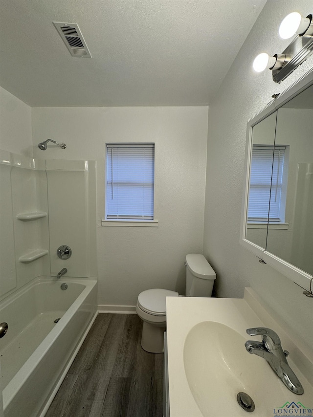 full bathroom with sink, bathing tub / shower combination, wood-type flooring, a textured ceiling, and toilet