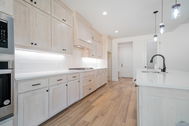 kitchen featuring built in microwave, sink, stainless steel gas cooktop, pendant lighting, and custom range hood