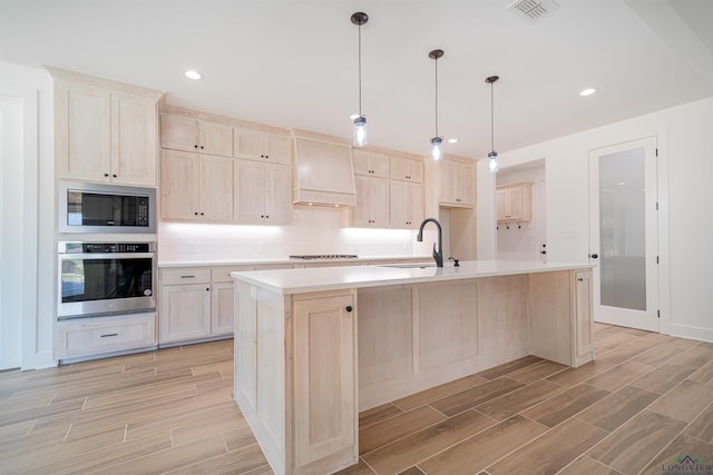 kitchen featuring a center island with sink, custom exhaust hood, built in microwave, and stainless steel oven