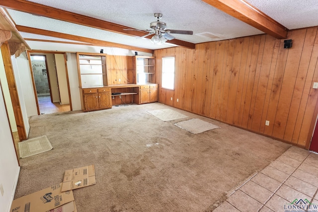 unfurnished living room with beam ceiling, a textured ceiling, wooden walls, and light carpet