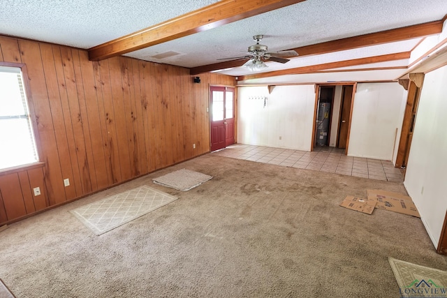 carpeted spare room featuring ceiling fan, wood walls, beamed ceiling, and a textured ceiling