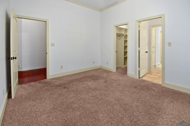 unfurnished bedroom featuring a closet, a walk in closet, light carpet, and crown molding