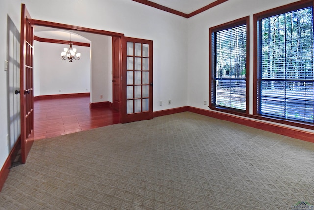 spare room featuring carpet, french doors, crown molding, and a chandelier