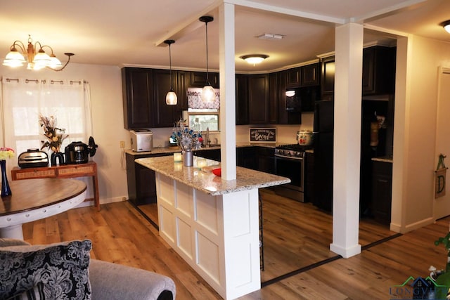 kitchen with light stone countertops, light wood-type flooring, decorative light fixtures, a notable chandelier, and stainless steel range with gas stovetop