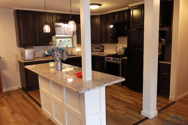 kitchen featuring stainless steel range with gas cooktop, sink, light hardwood / wood-style flooring, decorative light fixtures, and a kitchen island