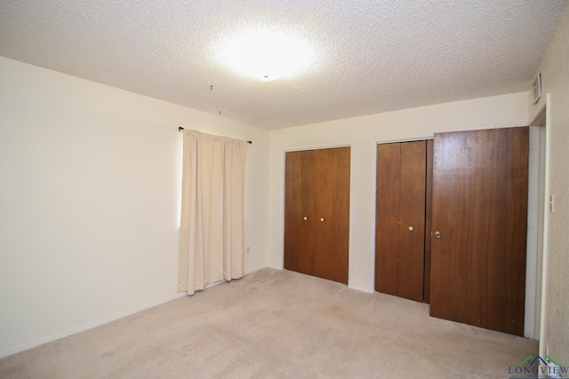 unfurnished bedroom with light colored carpet, a textured ceiling, and multiple closets