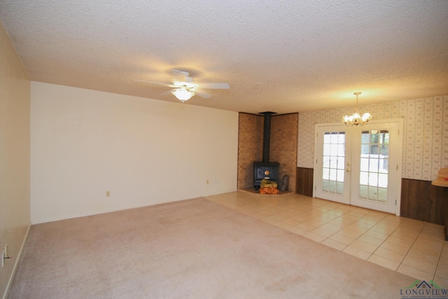 unfurnished living room featuring french doors, ceiling fan with notable chandelier, a textured ceiling, a wood stove, and light tile patterned flooring