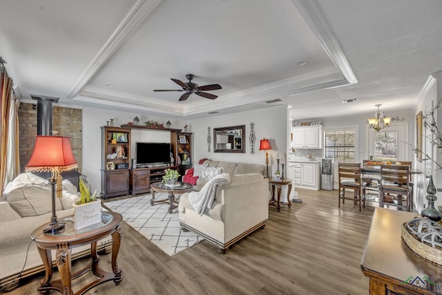 living room featuring crown molding, a wood stove, ceiling fan with notable chandelier, a raised ceiling, and light wood-type flooring