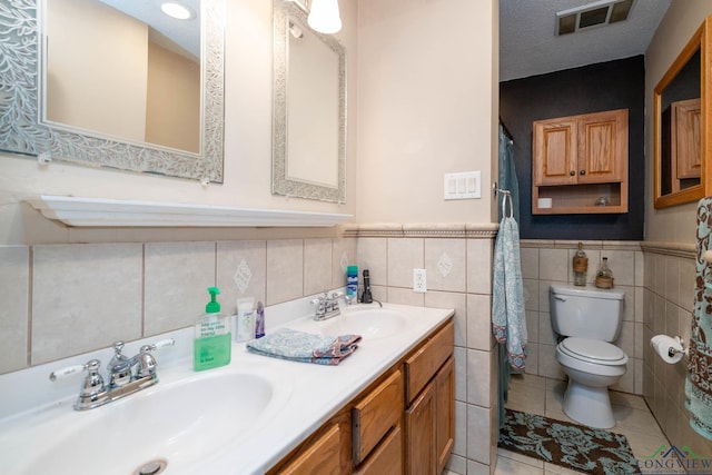 3365 Omie Dr, Longview, TX 75605 - bathroom featuring toilet, double vanity, tile walls, a wainscoted wall, and tile patterned floors