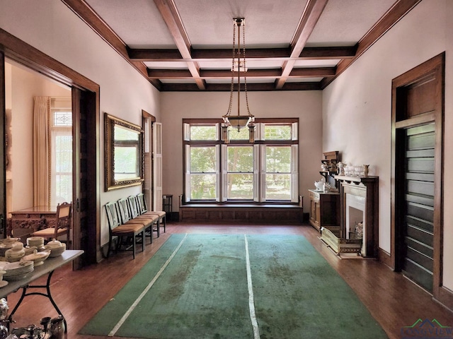 unfurnished dining area with coffered ceiling, dark hardwood / wood-style flooring, beamed ceiling, a chandelier, and a fireplace