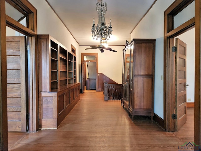 hallway with hardwood / wood-style flooring, crown molding, and an inviting chandelier