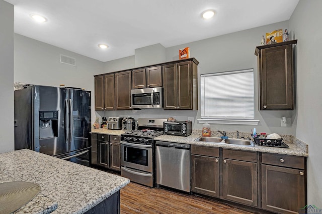 kitchen with light stone counters, dark brown cabinetry, sink, and appliances with stainless steel finishes