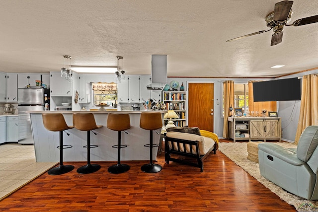 kitchen with a breakfast bar area, decorative light fixtures, stainless steel refrigerator, ceiling fan, and hardwood / wood-style floors