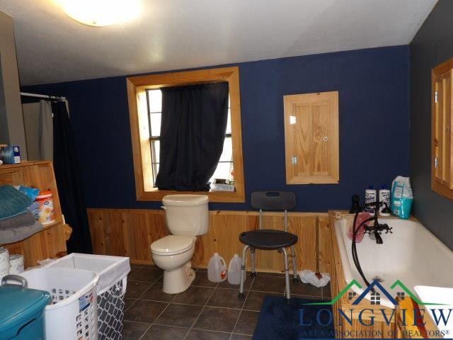 bathroom with tile patterned floors, wooden walls, toilet, and a tub