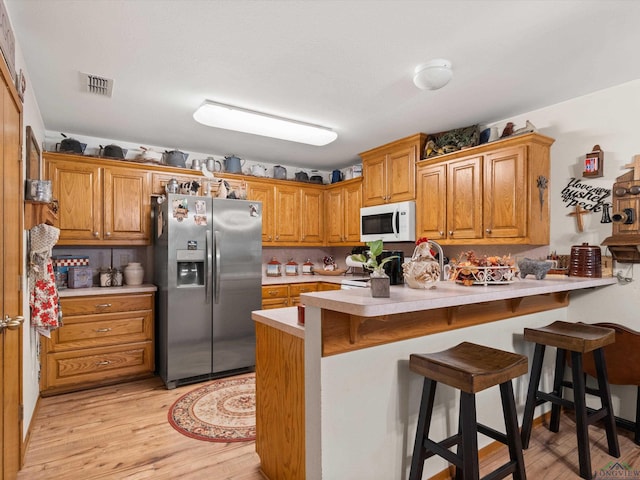 kitchen featuring a breakfast bar, stainless steel fridge with ice dispenser, kitchen peninsula, and light hardwood / wood-style floors