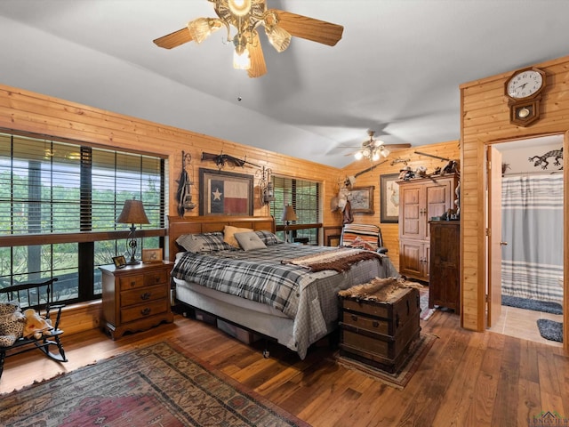 bedroom with ceiling fan, wood walls, wood-type flooring, and lofted ceiling