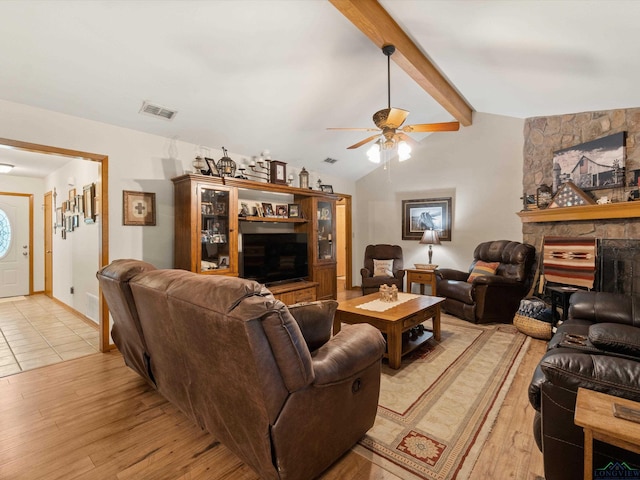 living room featuring vaulted ceiling with beams, ceiling fan, light hardwood / wood-style flooring, and a stone fireplace