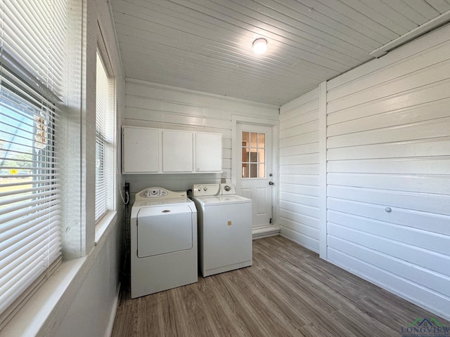 laundry room featuring cabinets, wooden walls, washing machine and dryer, and light wood-type flooring