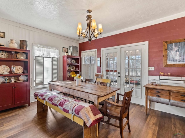 dining area with french doors, a textured ceiling, dark wood-type flooring, crown molding, and a notable chandelier