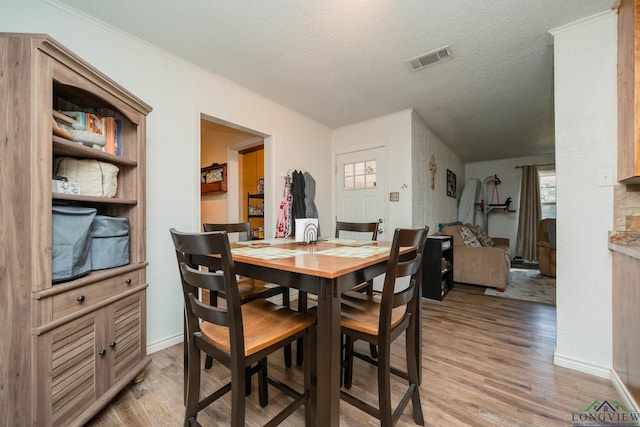 dining room with a textured ceiling, light hardwood / wood-style flooring, and ornamental molding