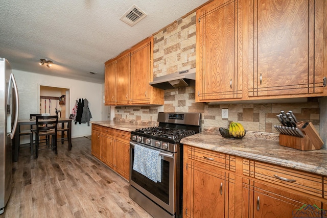 kitchen featuring stainless steel appliances, a textured ceiling, light hardwood / wood-style flooring, decorative backsplash, and light stone countertops