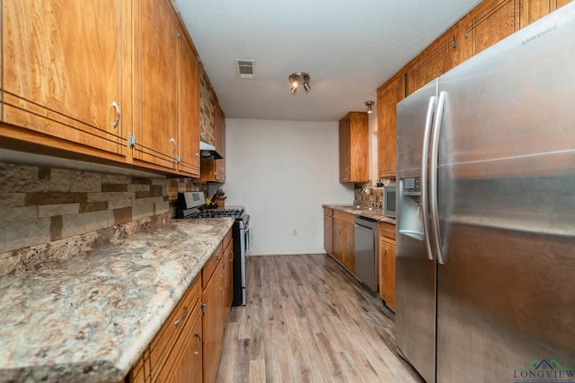 kitchen with light hardwood / wood-style floors, stainless steel appliances, a textured ceiling, sink, and backsplash